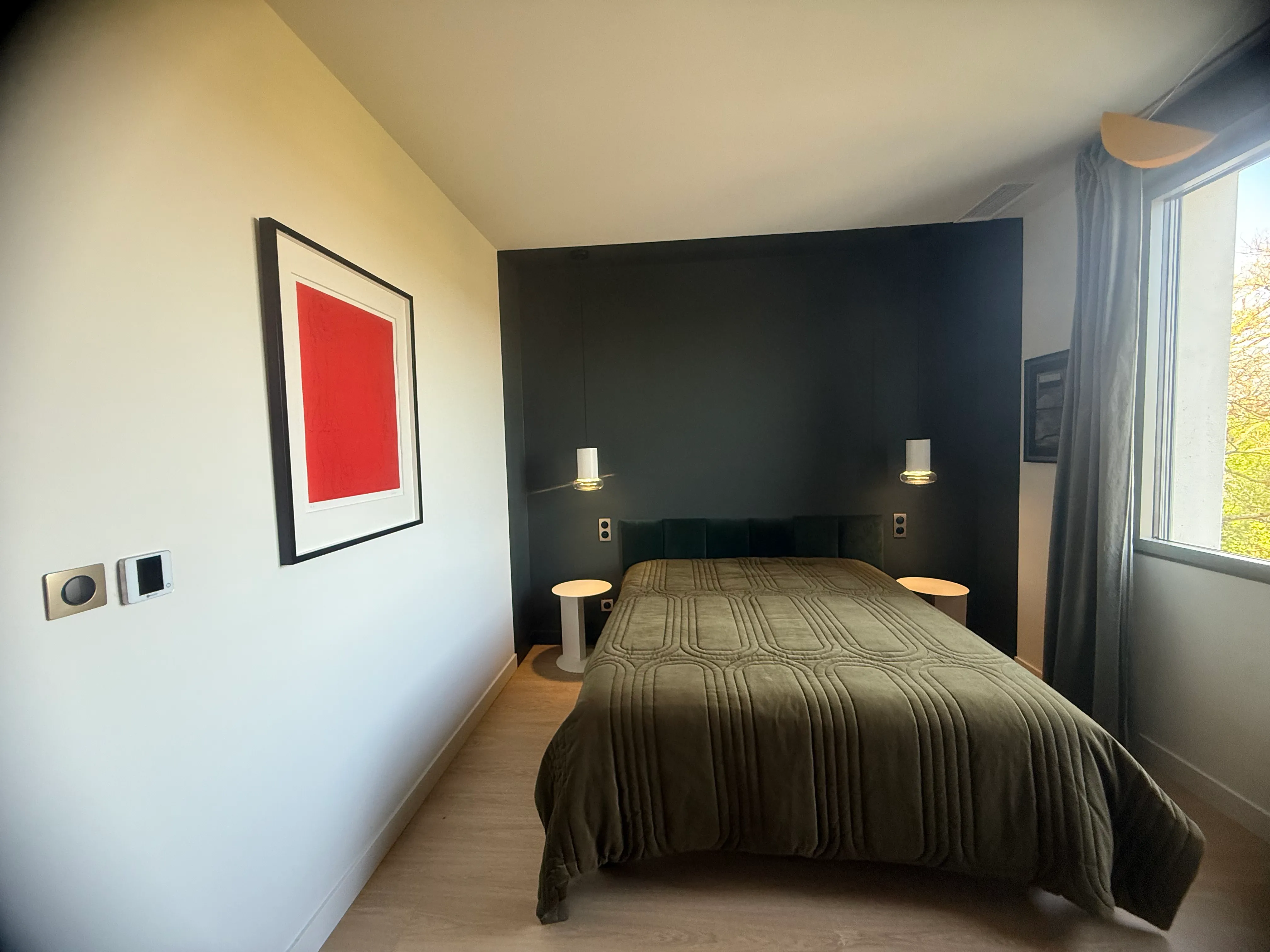 Chambre avec mur accent vert très foncé, parquet clair, appliques chromées et linge de lit kaki — réalisation peinture intérieure LK Peinture