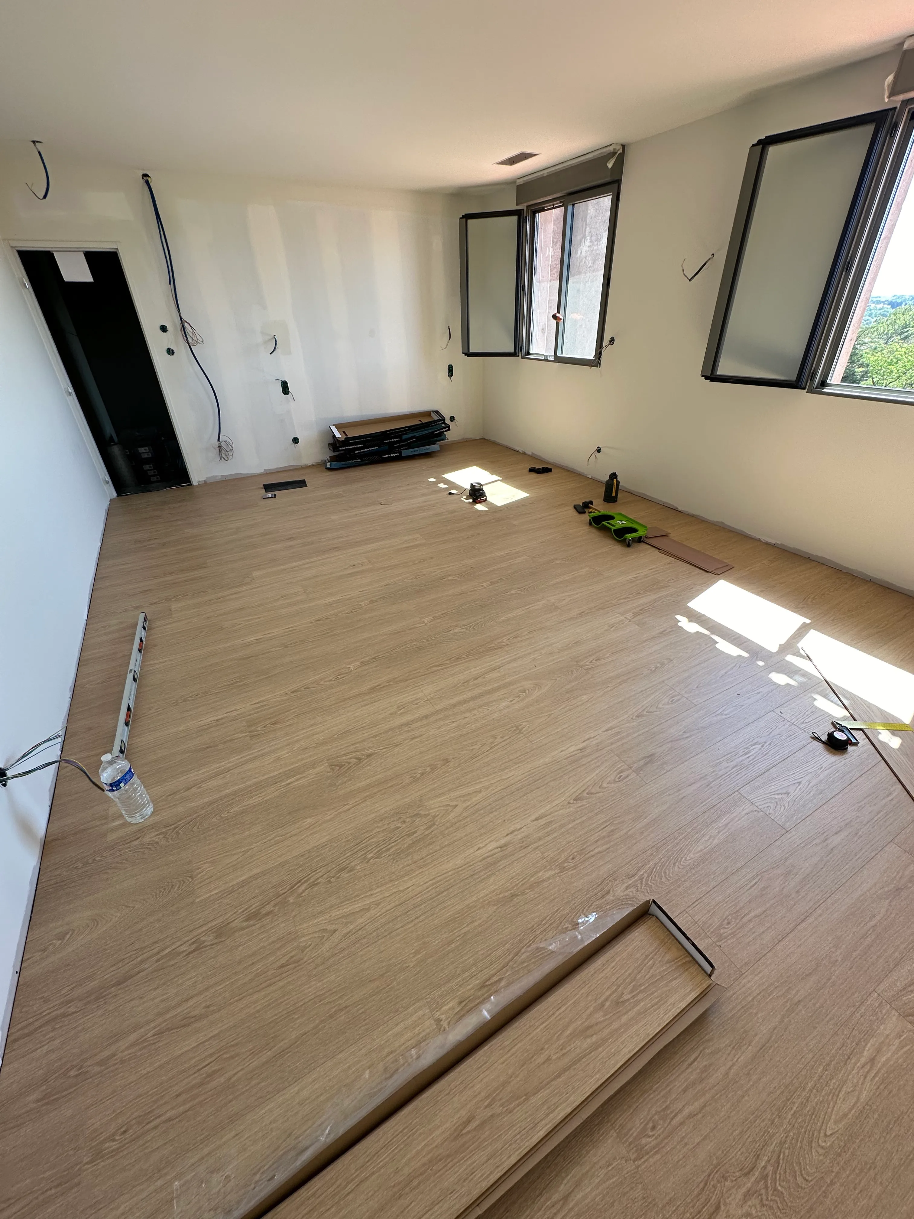Chantier de pose de parquet en cours dans une pièce lumineuse, lames en cours d'assemblage